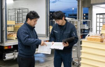 早朝のパン配送センターで給与内訳表とルート勤務表を照合するドライバーと責任者